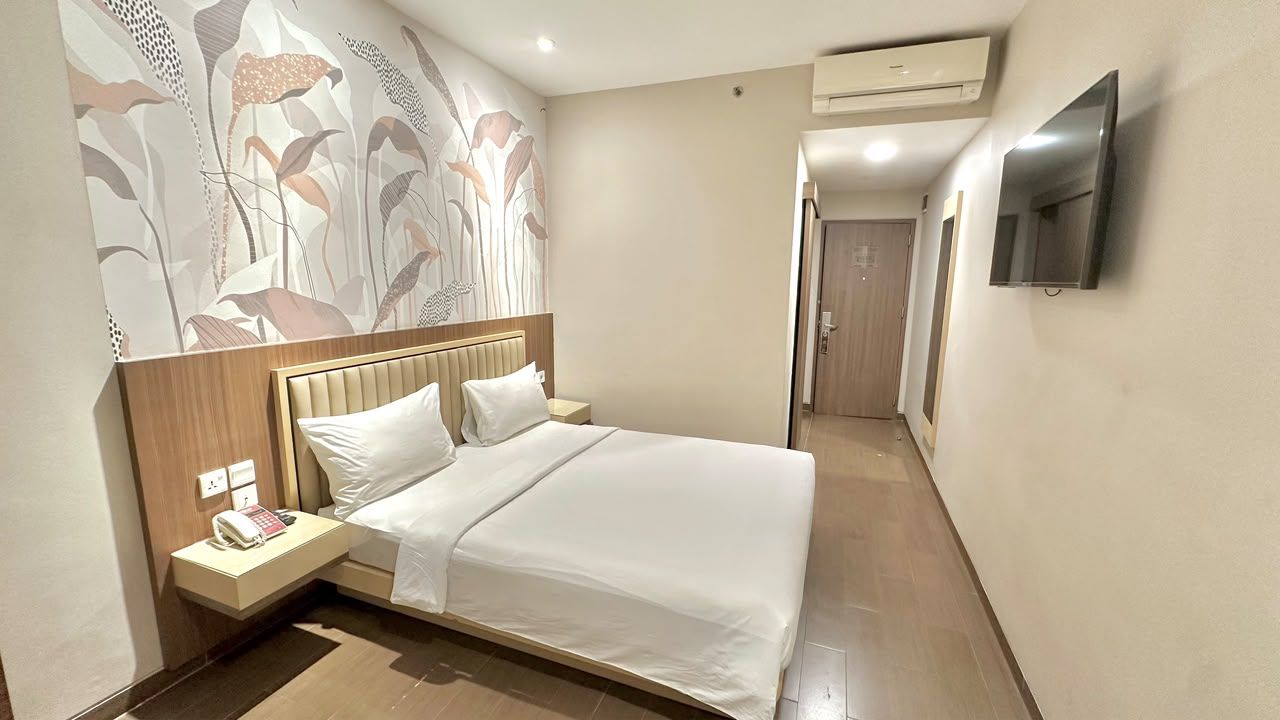A hotel room with a bed, bedside table, and a wall-mounted TV.