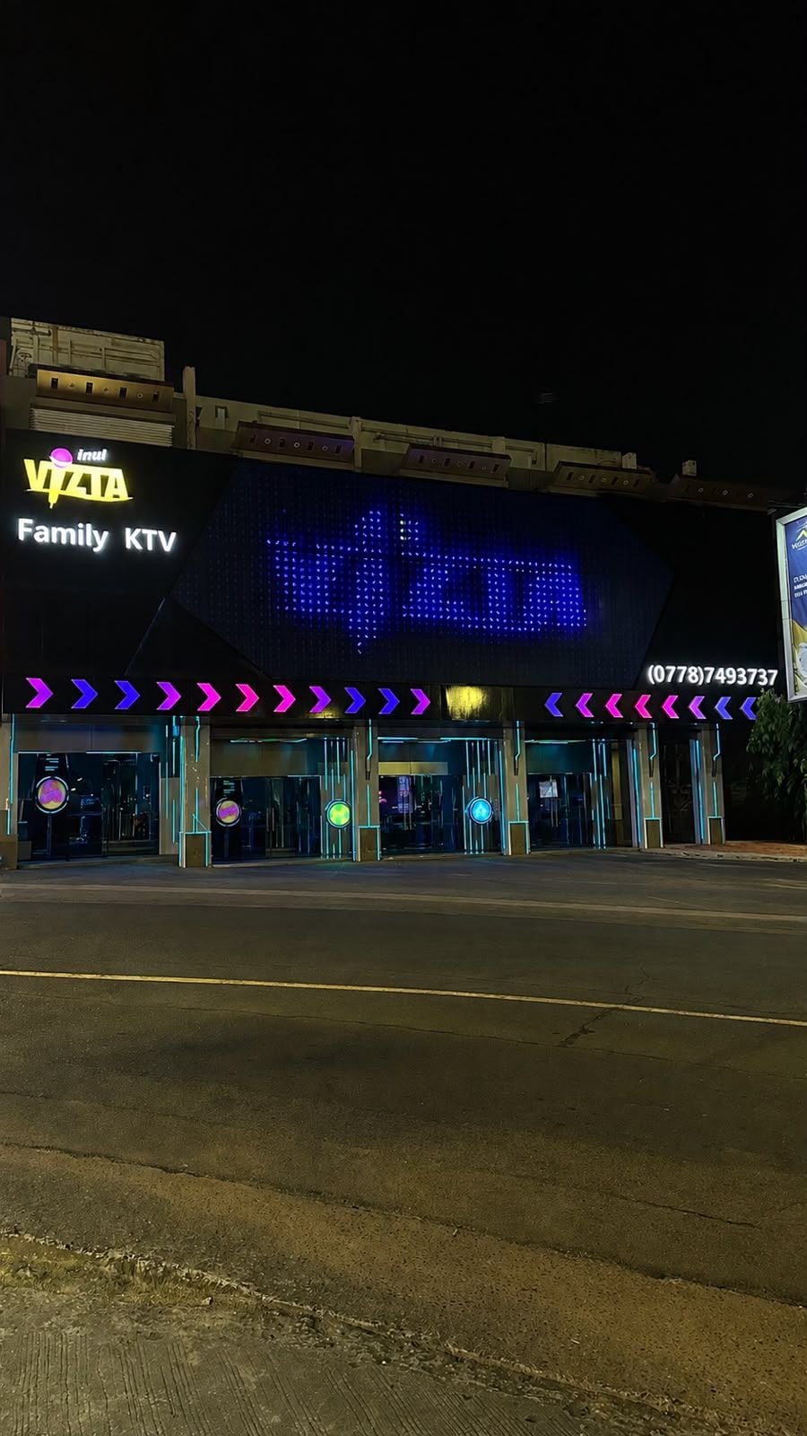 Ein Gebäude mit einer digitalen Anzeige, auf der 'VIZTA Family KTV' steht, und einer Kontaktnummer.