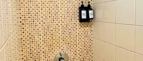 A shower with mosaic tiles, a handheld showerhead, and two bottles of body wash.