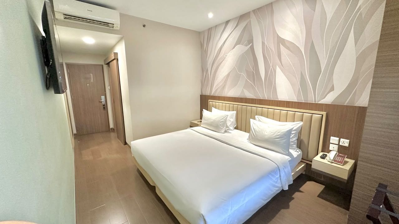 A hotel room with a large bed, a bedside table with a lamp, and a wall-mounted TV.