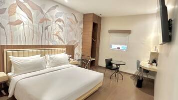 Quarto de hotel com uma cama grande, escrivaninha, cadeira, televisão e parede com padrão floral.