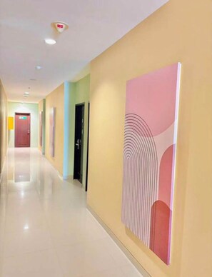 Un long couloir bien éclairé, avec des portes d’un côté et une grande œuvre d’art abstrait de l’autre.