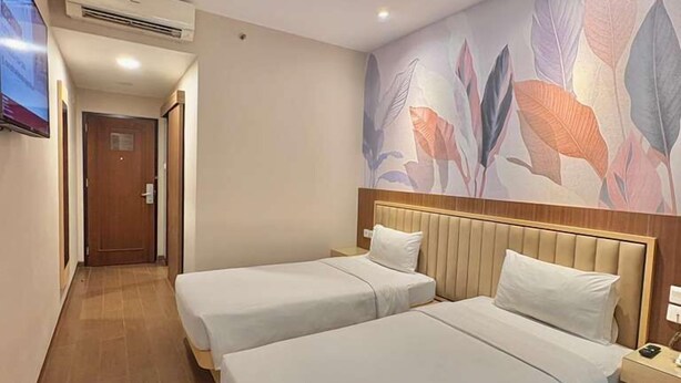 Ein Hotelzimmer mit zwei Betten, einem an der Wand befestigten Fernseher und einem floralen Wandbild.
