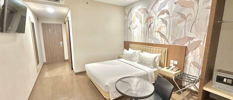 Une chambre d’hôtel avec un lit, une petite table, une chaise, un téléviseur et un mur orné d’un motif floral.