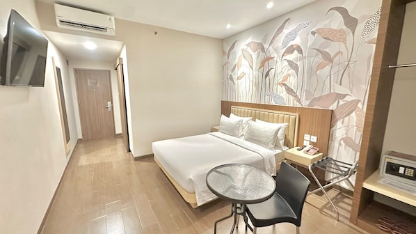 Habitación de hotel con cama, una mesita, una silla, televisor y un papel tapiz con motivos florales.