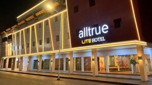 Een hotel met een opvallend bord waarop 'alltrue LITE HOTEL' staat, en een moderne gevel met verlichte lijnen.