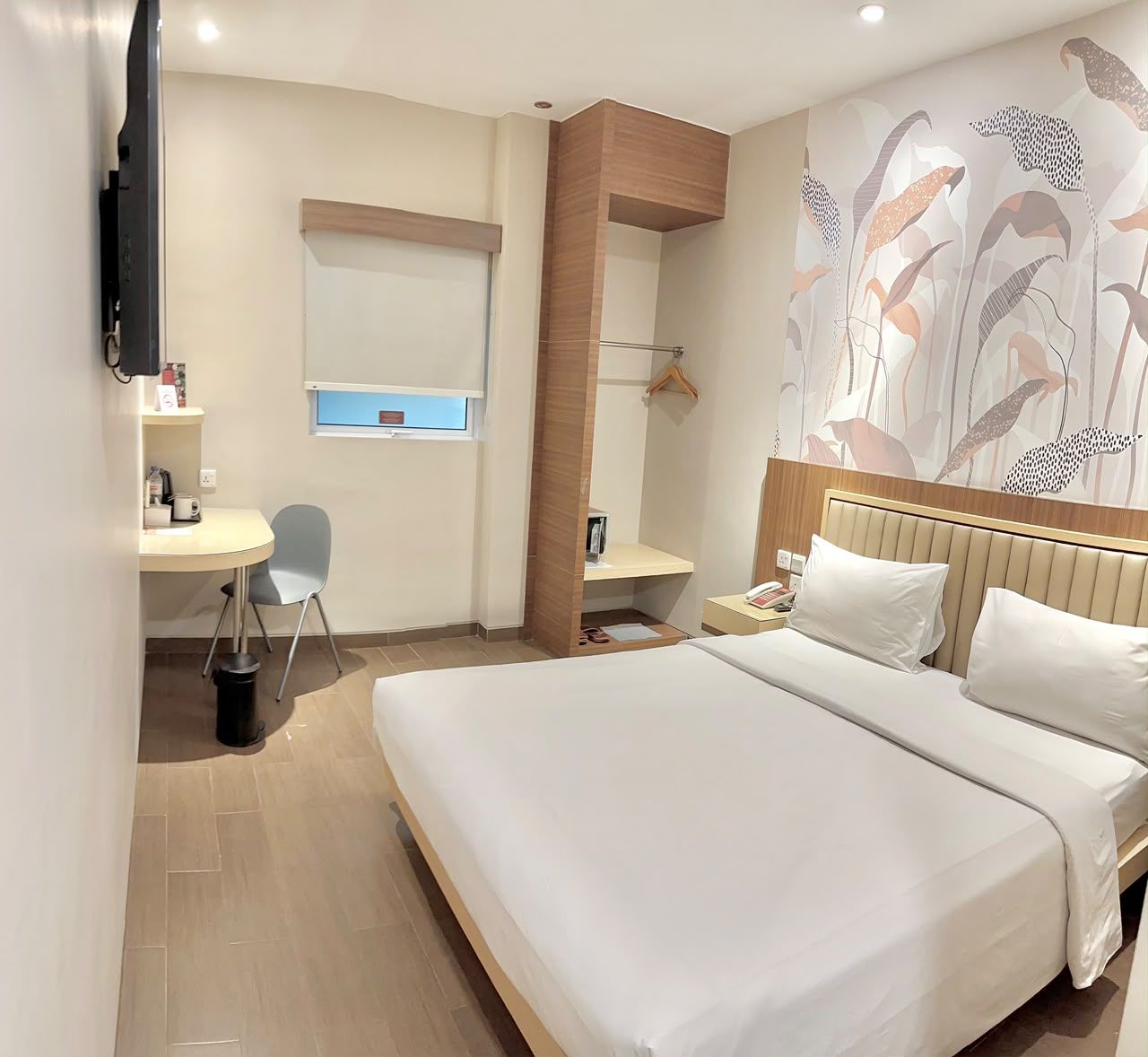 A hotel room with a bed, a desk, a chair, a television, and a wall with a floral pattern.