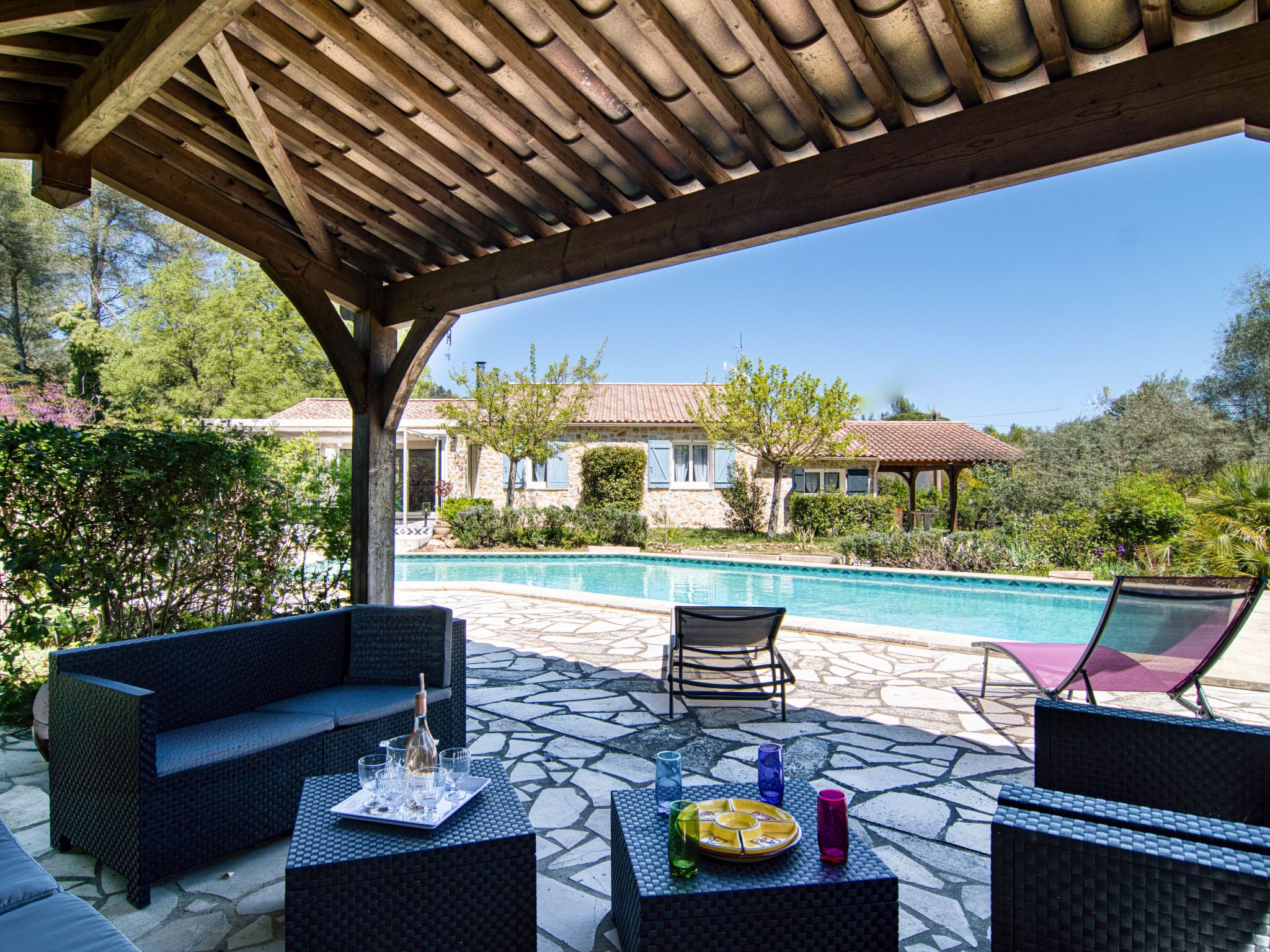 A covered outdoor area with a pool, wicker furniture, and a stone patio.