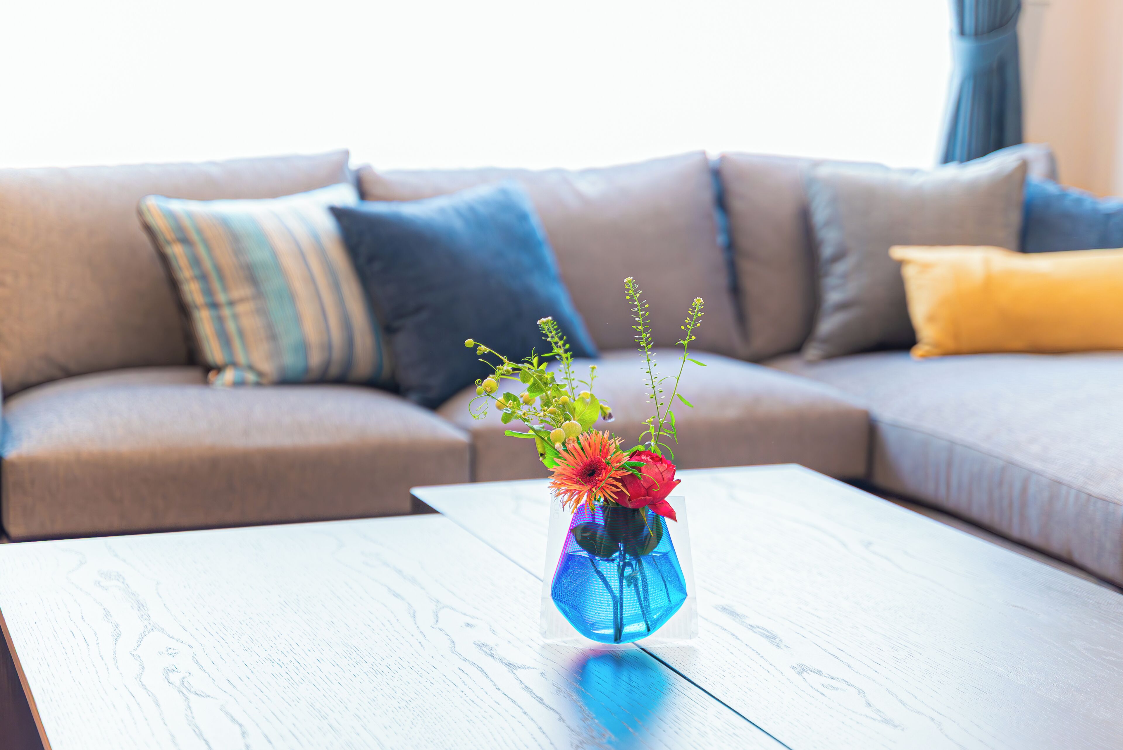 A living room with a sofa, a coffee table, and a vase with flowers.