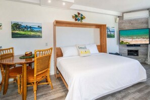 A hotel room with a bed, wooden headboard, a dining table with chairs, and a television on the wall.