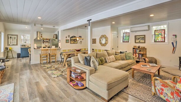 A spacious living area with a large sofa, a dining table, and a kitchen in the background. - Cozy Farmhouse on 1 acre- Stargaze in the Hot tub (Bend)