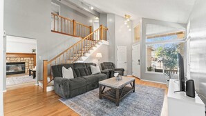 Un salon avec un escalier, une cheminée, un canapé, une table basse et un téléviseur.