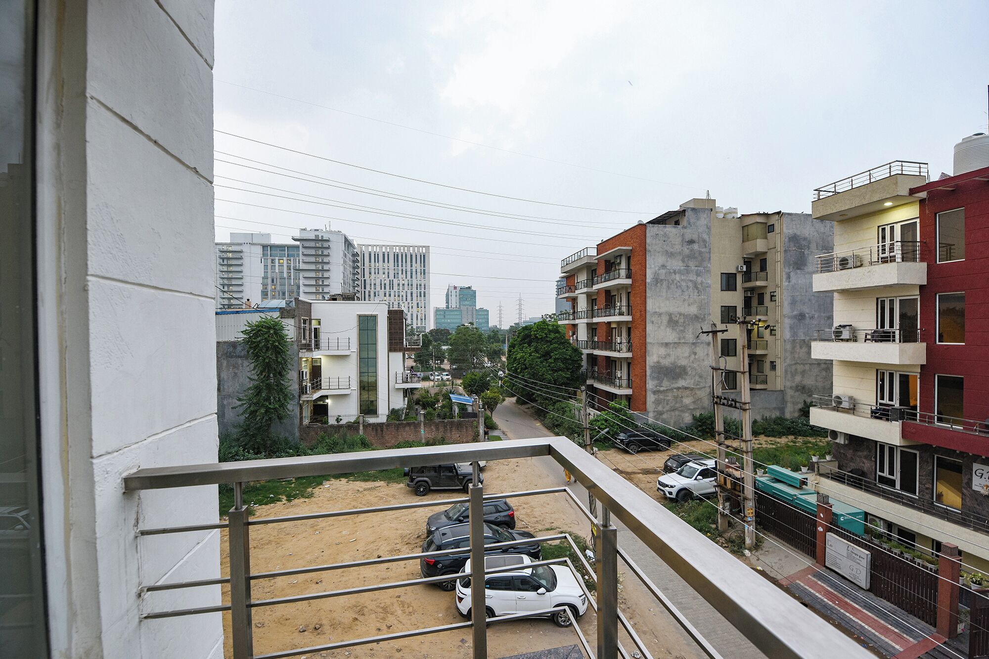 Zona residencial com edifícios altos, estrada de terra e carros estacionados.