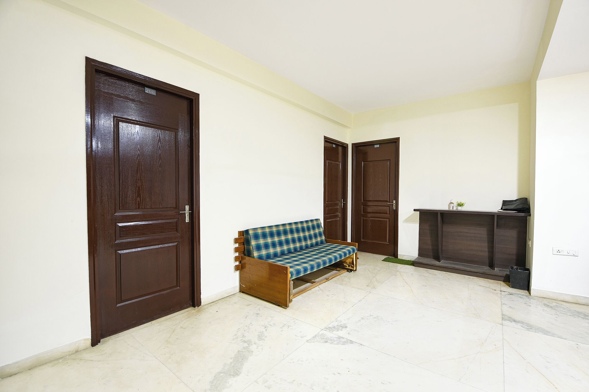 Un couloir avec deux portes en bois, un banc et un petit bureau agrémenté d’une plante.