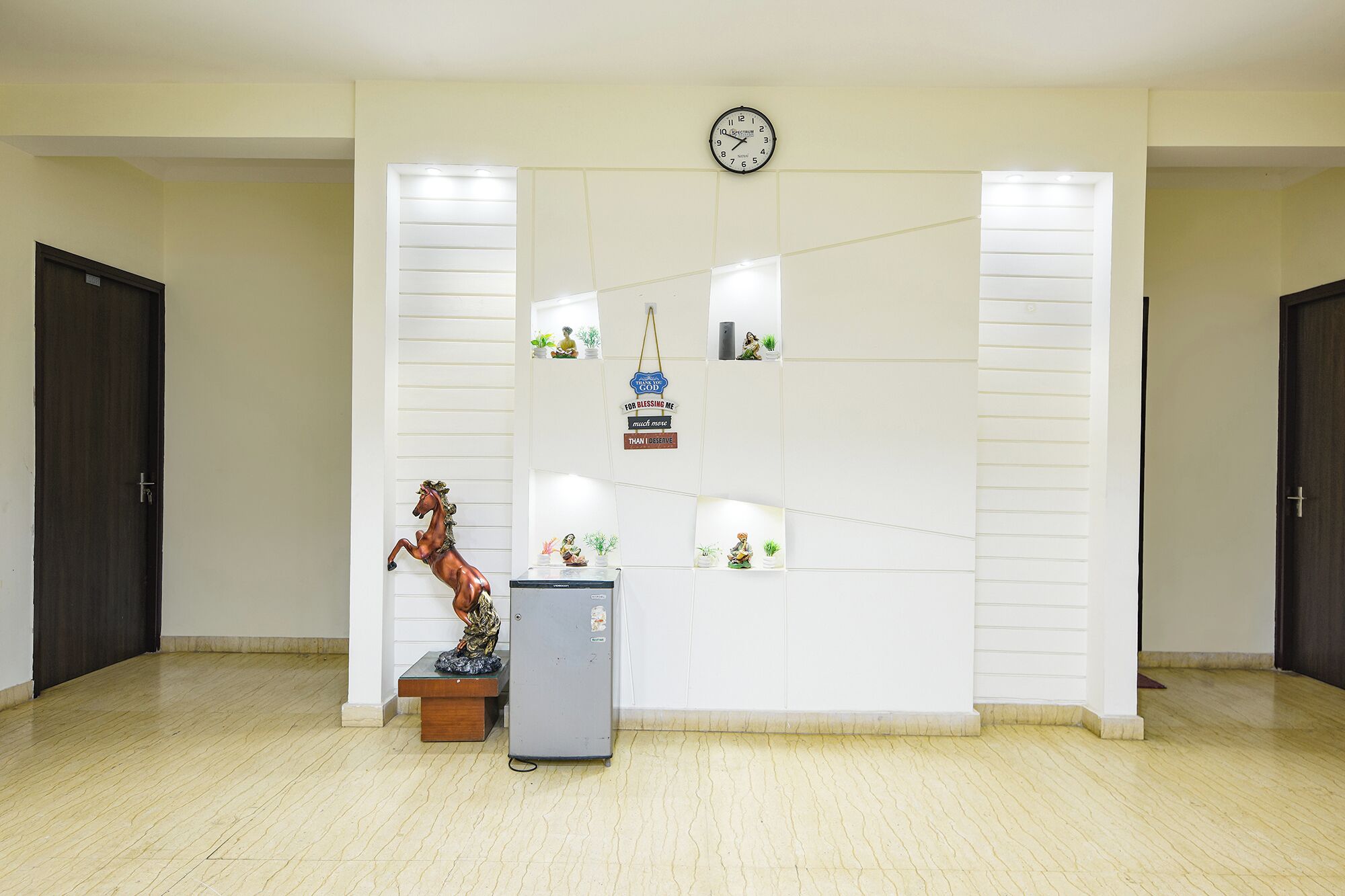 A reception area with a clock, a statue, and a refrigerator.