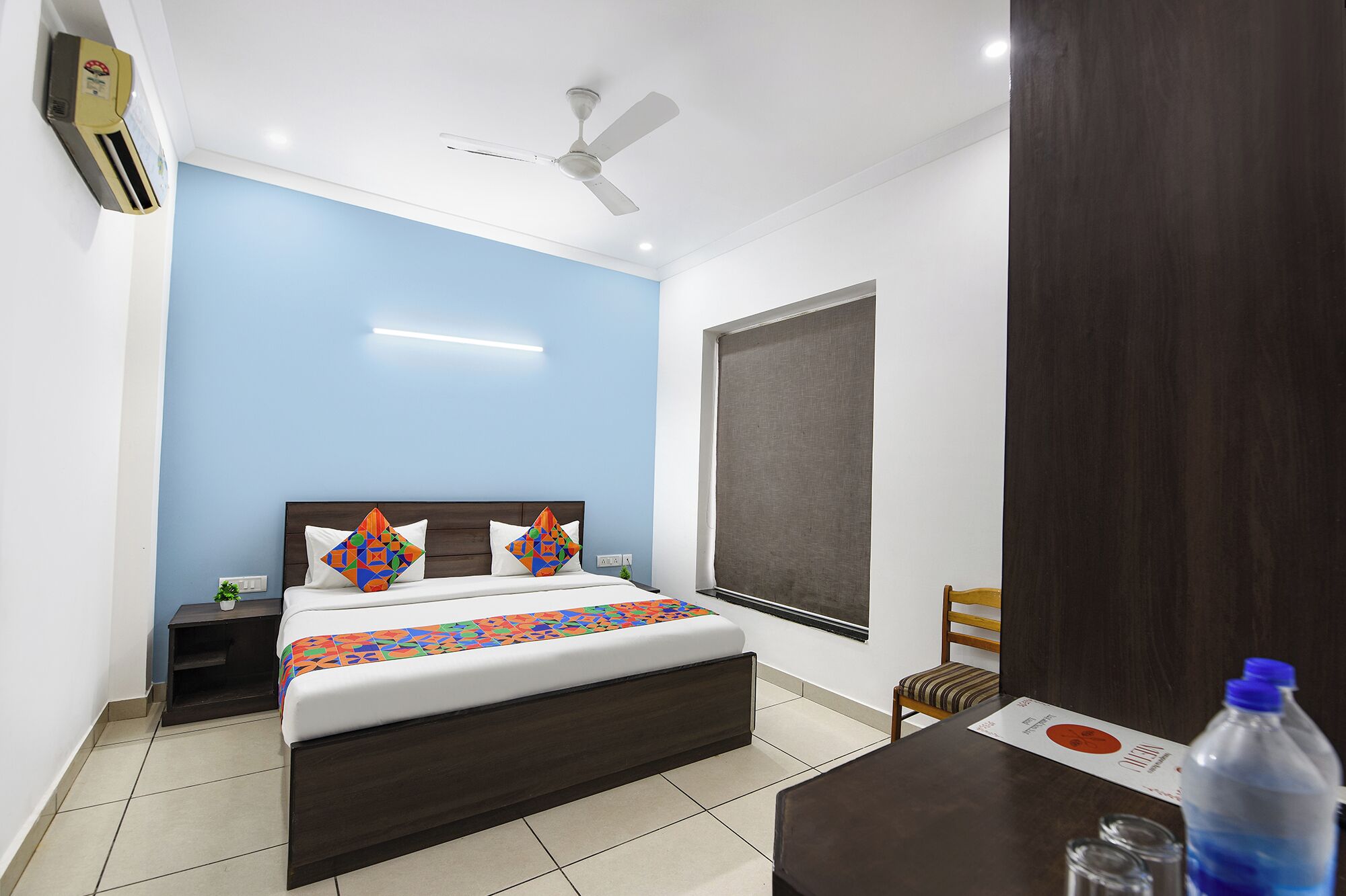 A bedroom with a bed, bedside tables, a ceiling fan, a window with a blind, and a wooden door.