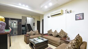 A living room with a sofa set, a coffee table, and a staircase leading to an elevator. - Gazelle By Wonderland (Gurugram)