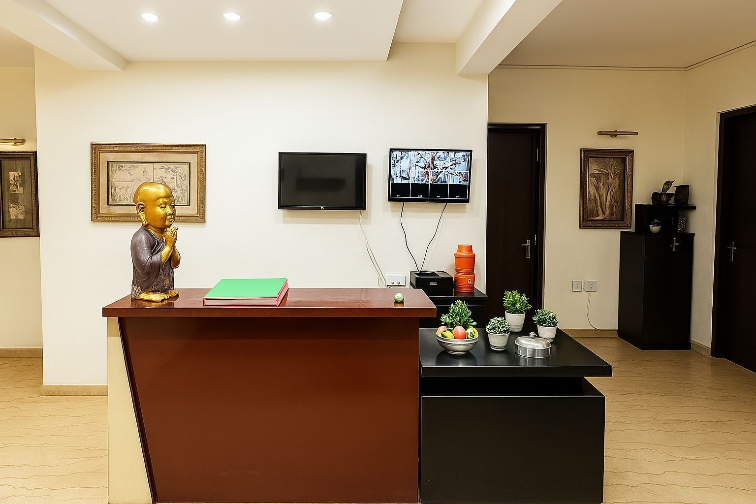 A reception area with a wooden desk, a Buddha statue, a framed picture, a television, and potted plants.