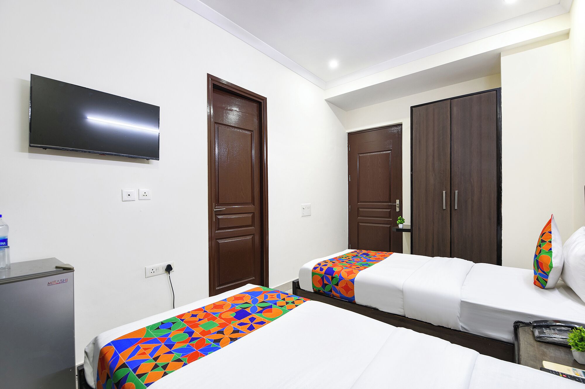 A hotel room with two beds, a TV mounted on the wall, and a minibar.