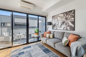 Ein modernes Wohnzimmer mit grauem Sofa, einem großen Fenster und einem raumhohen Blick auf eine Stadtlandschaft.