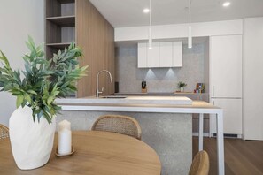 A modern kitchen with a central island, white cabinets, and a dining area with a round table and chairs. - Trendy 1-Bed Retreat in Fremantle with Rooftop (North Fremantle)