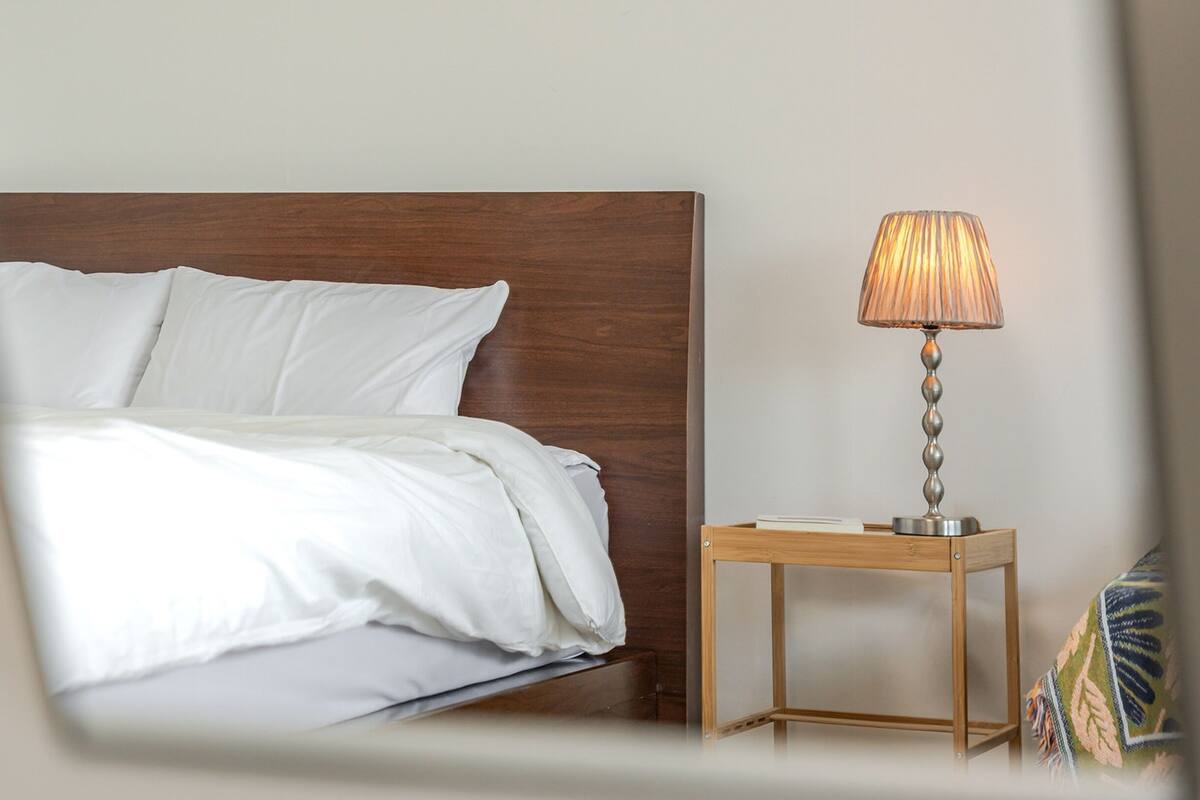 Ein ordentlich bezogenes Bett mit weißen Leinen und einem Holz-Kopfteil.