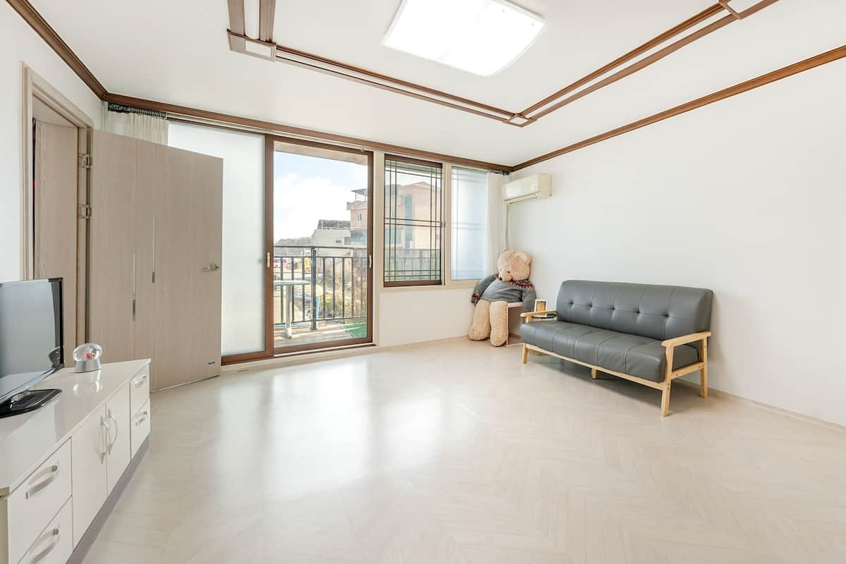Ein geräumiges Wohnzimmer mit einem grauen Sofa, einer Holzkommode und einem großen Fenster mit Blick ins Freie.