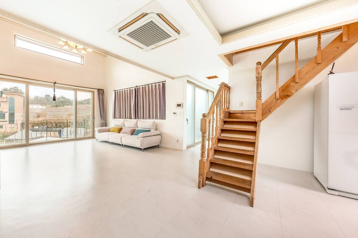 Ein geräumiger Wohnbereich mit einer Holztreppe, großen Fenstern und einem weißen Sofa.