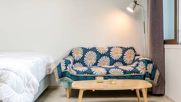 Una stanza con un letto, un divano con una coperta floreale, un piccolo tavolino con una tazza e una candela, e una lampada da terra.