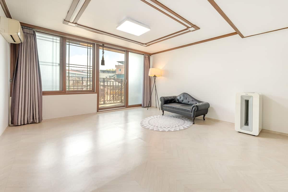 Ein geräumiger Raum mit einer großen Schiebeglasdoor, einer Stehlampe, einer schwarzen Ledersofa und einem weißen Luftreiniger.