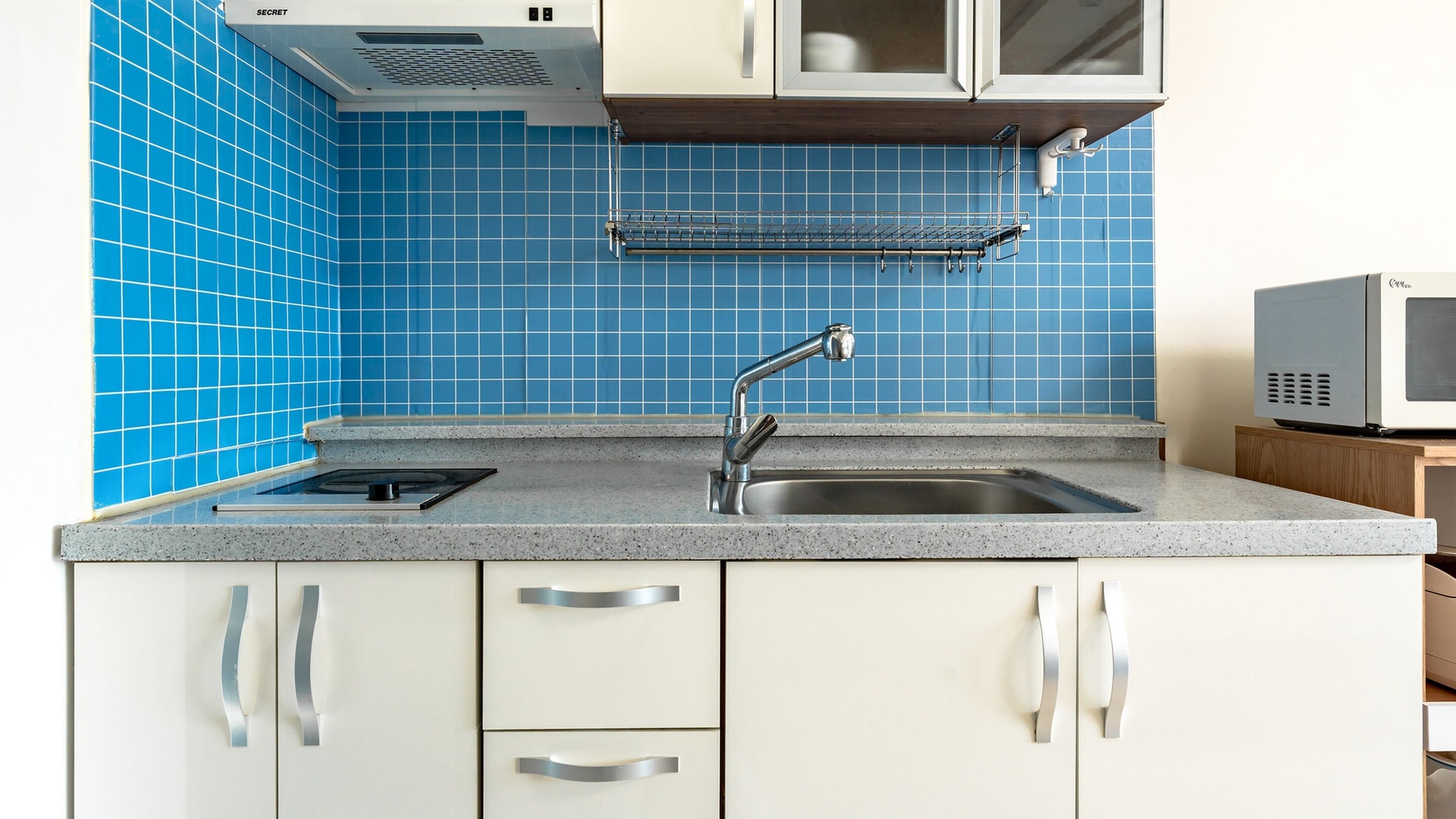 A kitchen with a stainless steel sink, white cabinets, and blue tiled backsplash.