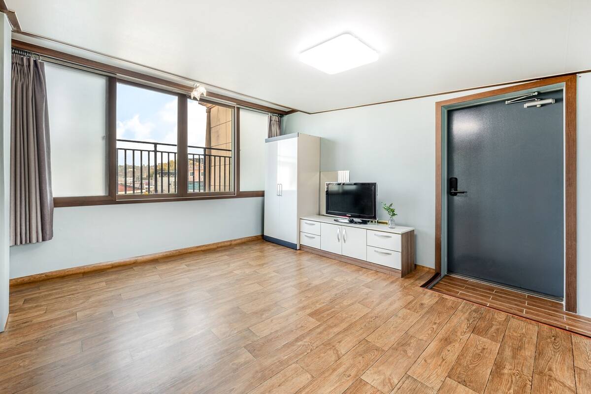 Ein Zimmer mit großem Fenster, Fernseher, Kleiderschrank und Tür.