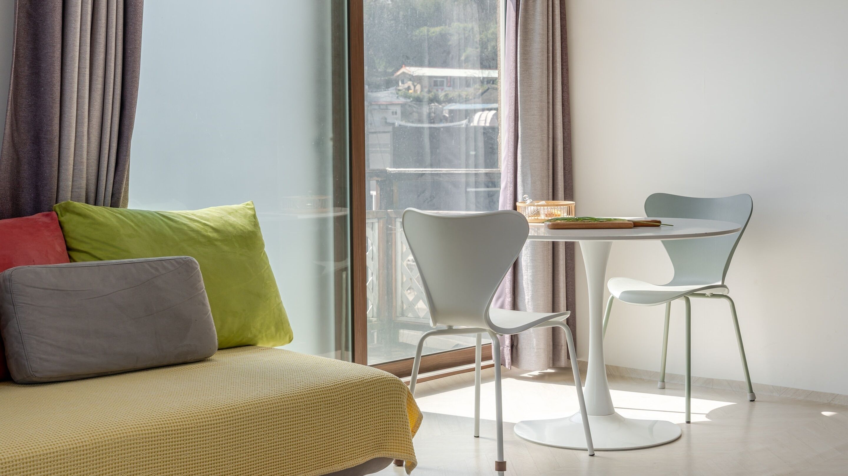 A modern room with a bed, two chairs, a small table, and a view through a large window.
