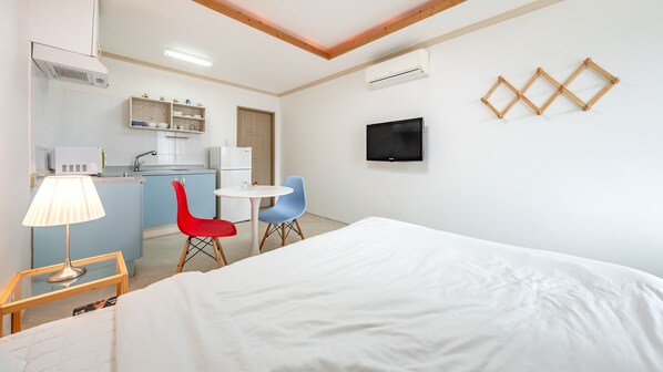 A hotel room with a bed, a desk with a lamp, a TV, and a kitchenette.