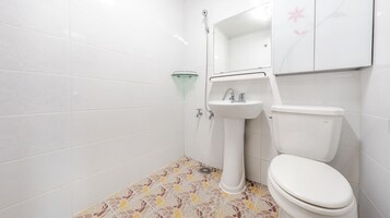 Baño con azulejos blancos, lavamanos de vidrio, inodoro y ducha.