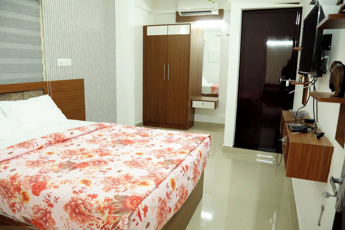 A bedroom with a bed, a wardrobe, a mirror, a television, and a desk.