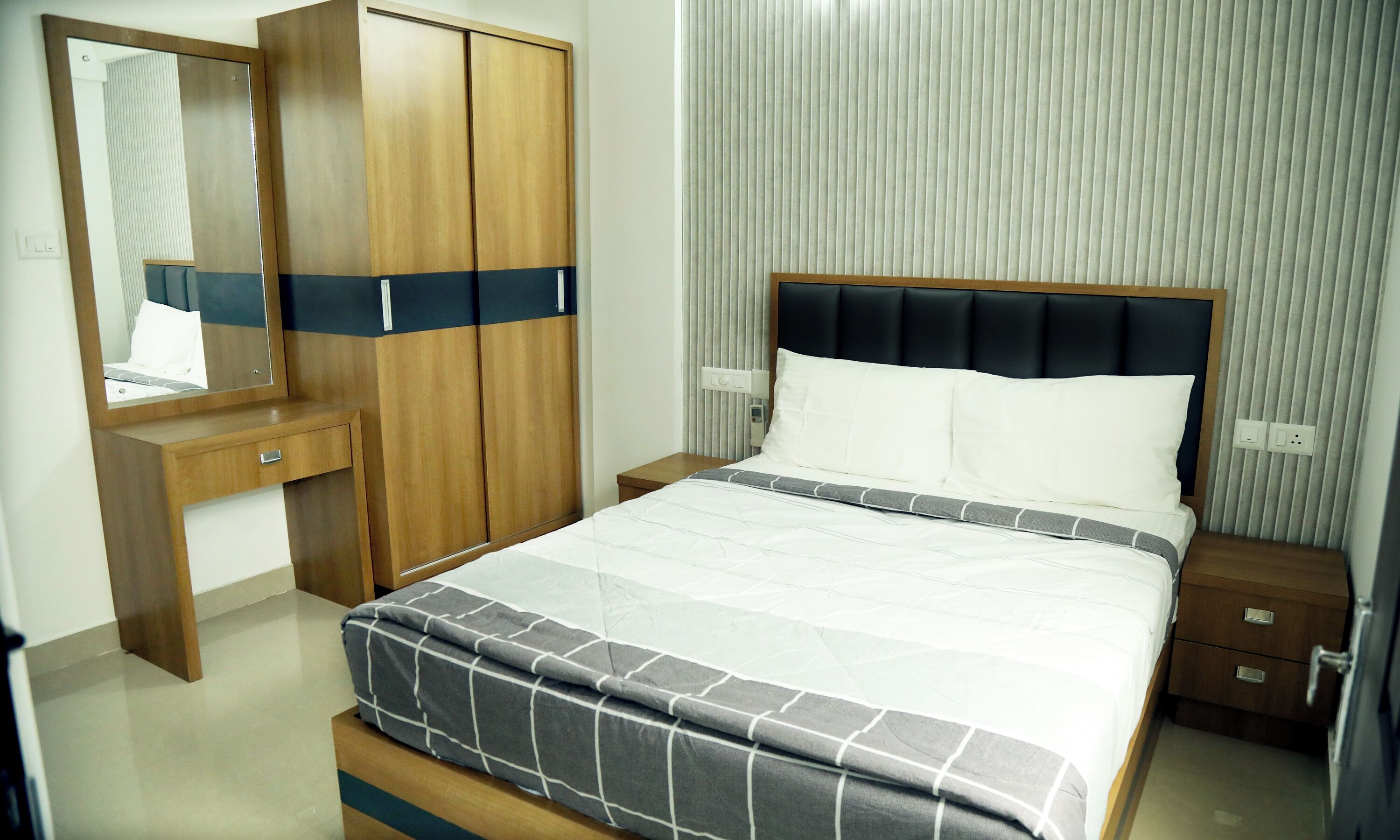 A hotel room with a bed, a wardrobe, a bedside table, and a mirror.