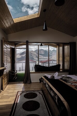 A room with a bed, a window with a view of mountains, a skylight, and a hanging light fixture.