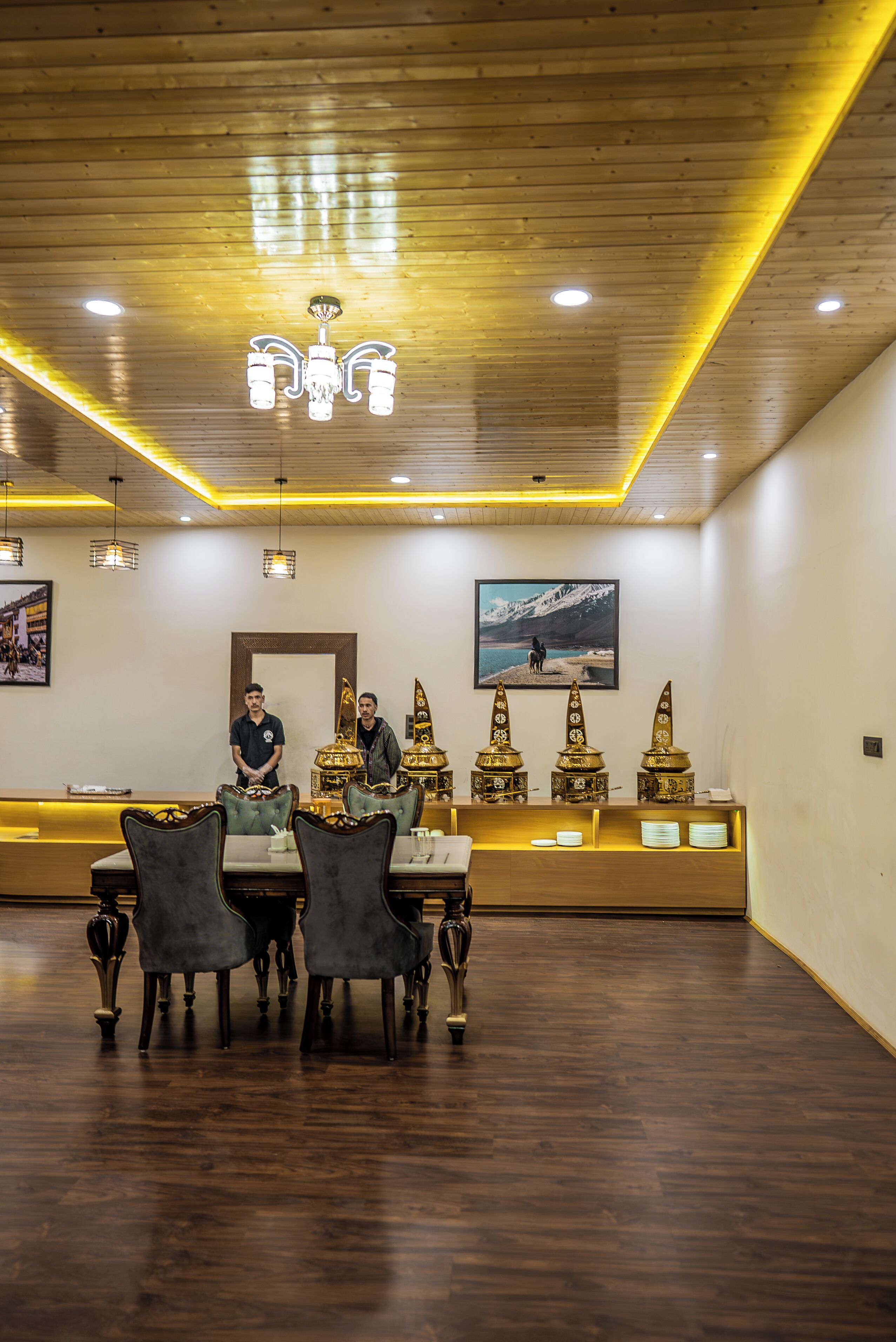 A dining area with wooden tables and chairs, a chandelier, and decorative items on a counter.