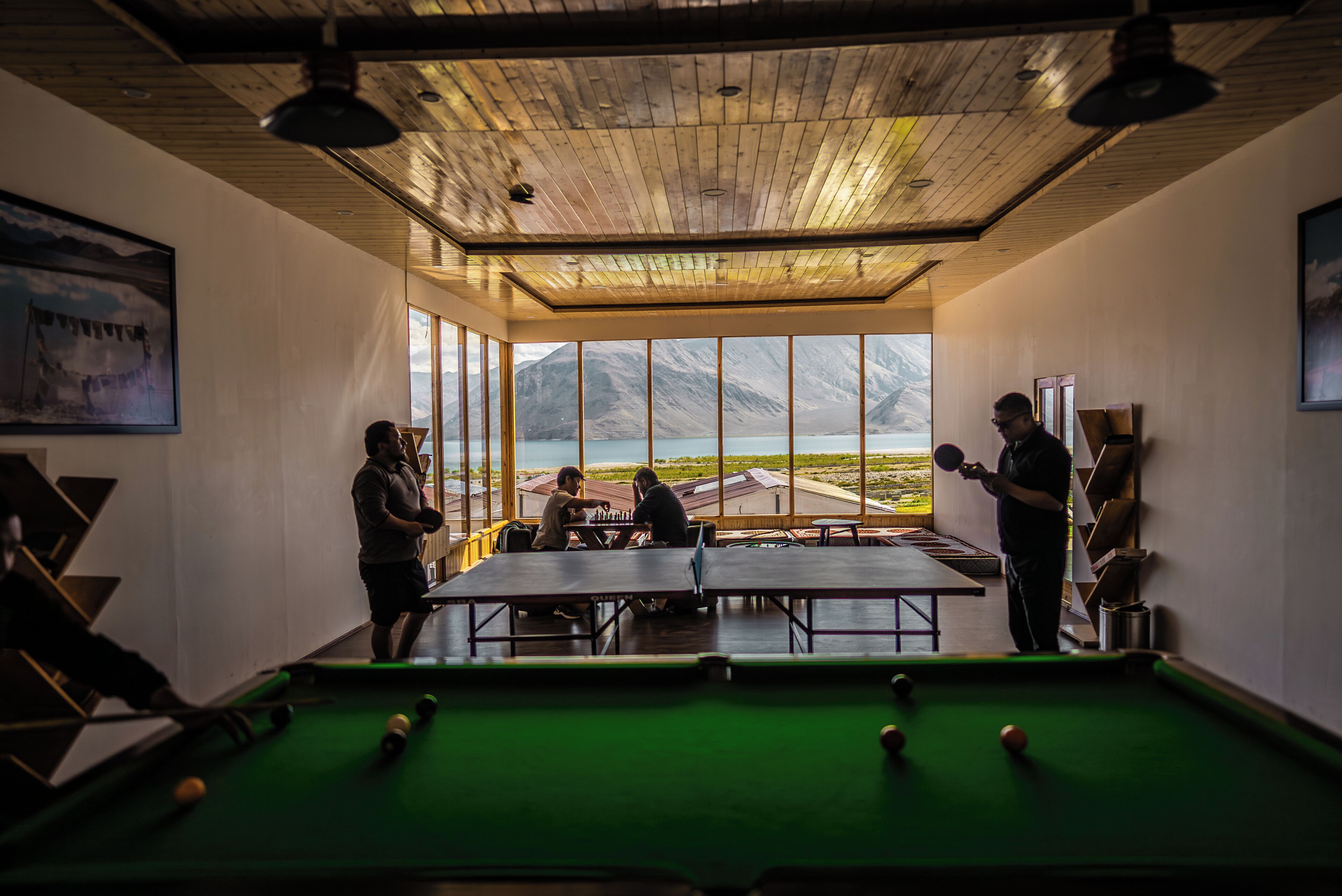 A pool table in a room with large windows and wooden ceiling.