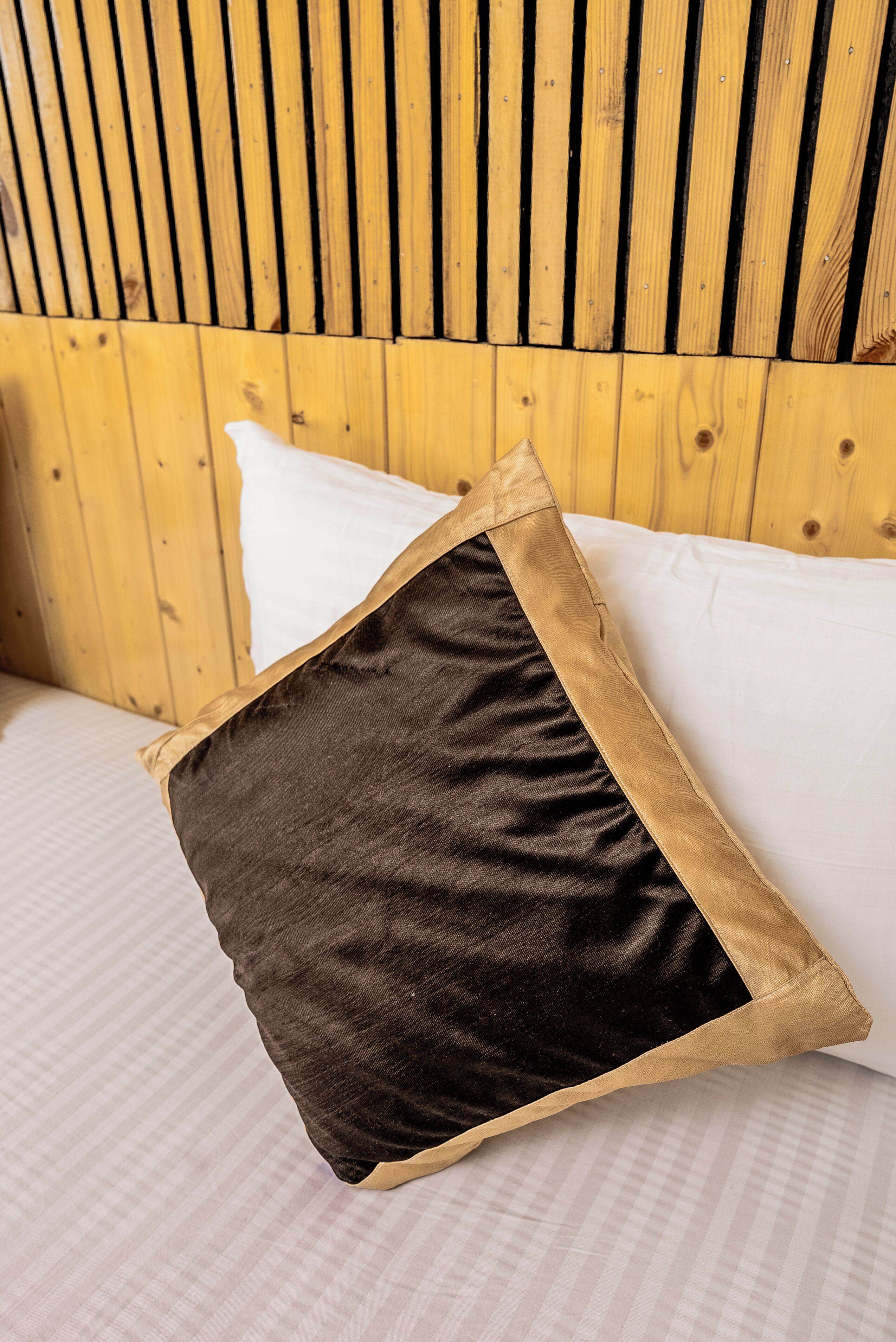 Ein Bett mit einem hölzernen Kopfteil, einem weißen Kissen und einem schwarzen Kissen mit goldener Zierleiste.