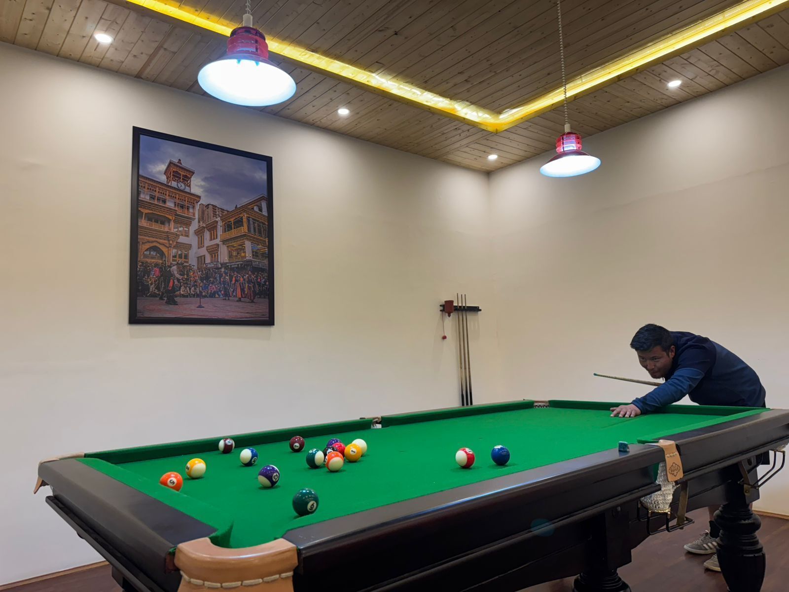 A pool table with balls, a billiard cue, and a framed picture of a building on the wall.