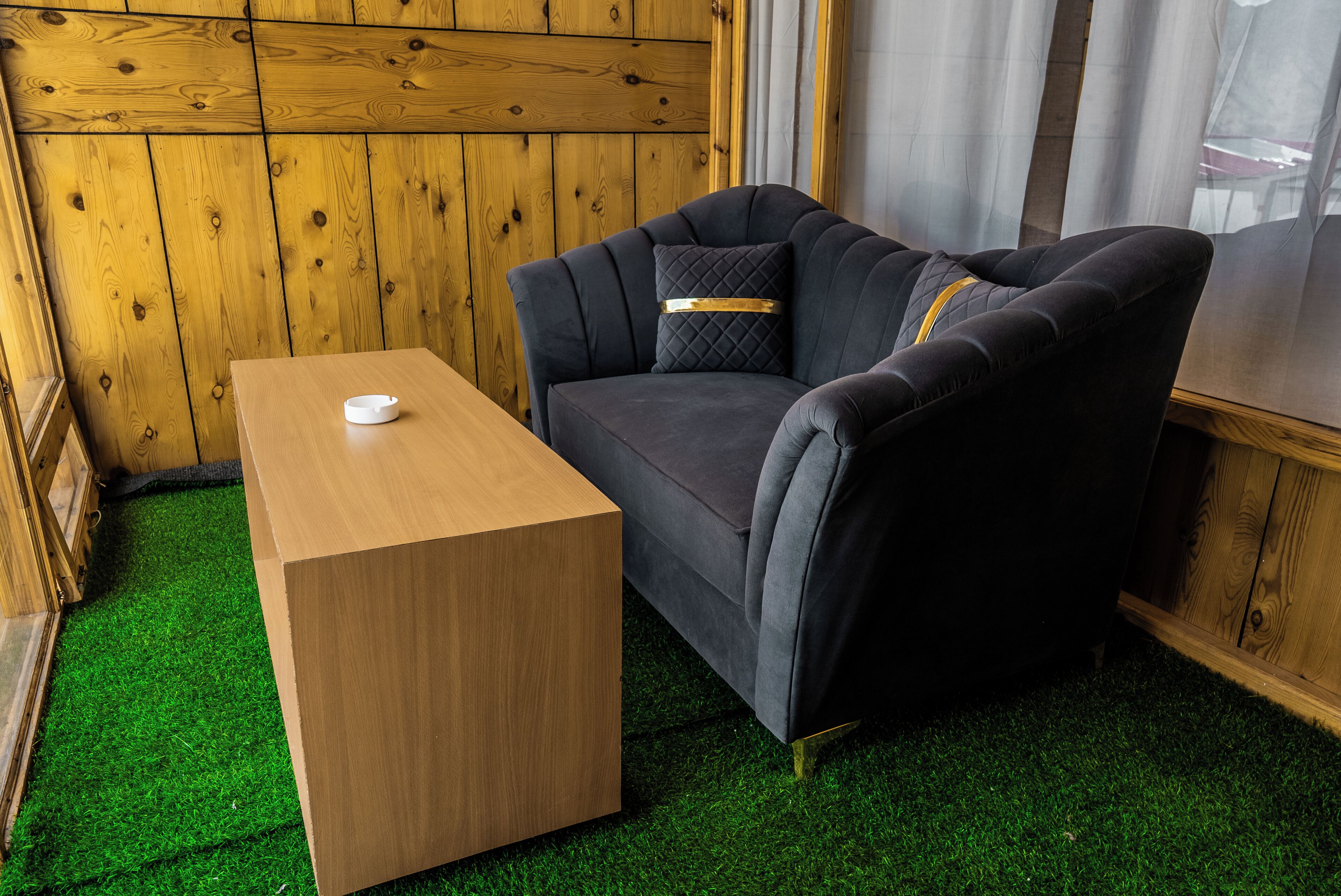 Una habitación con un panel de madera, un sofá tapizado oscuro con un cojín acolchado y una mesita de madera.