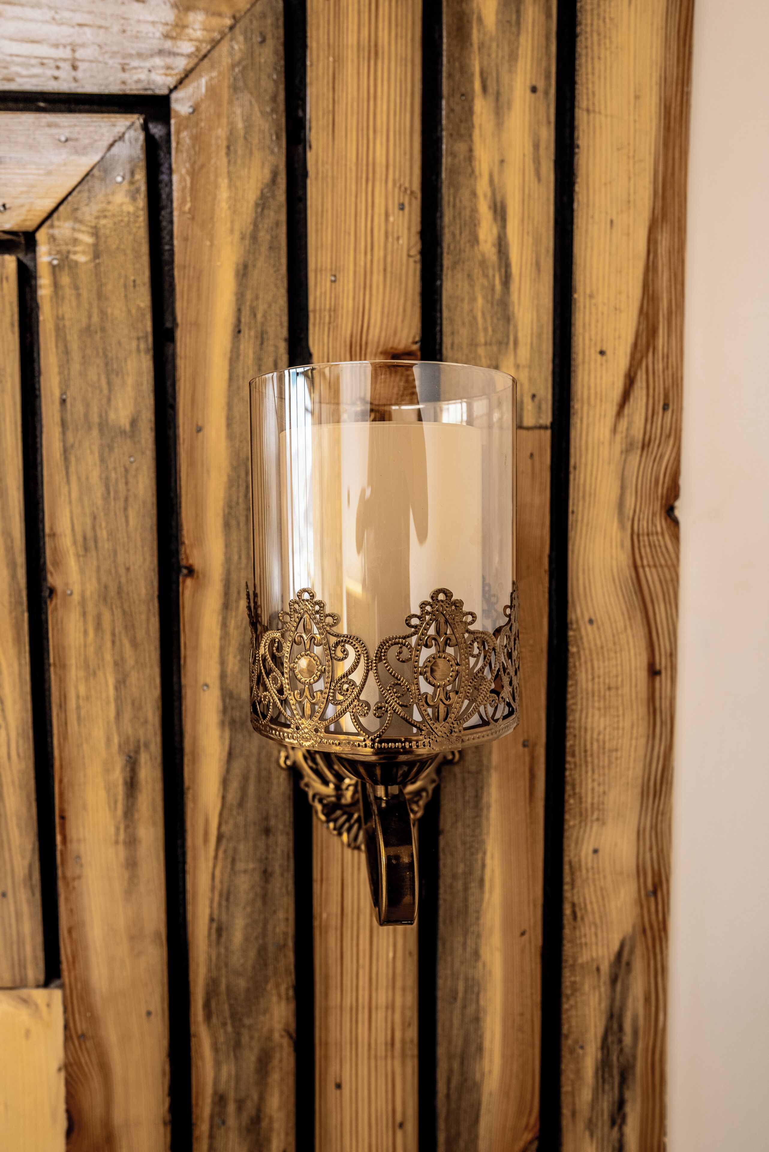 A wall-mounted candle holder with ornate metalwork against a wooden panel background.