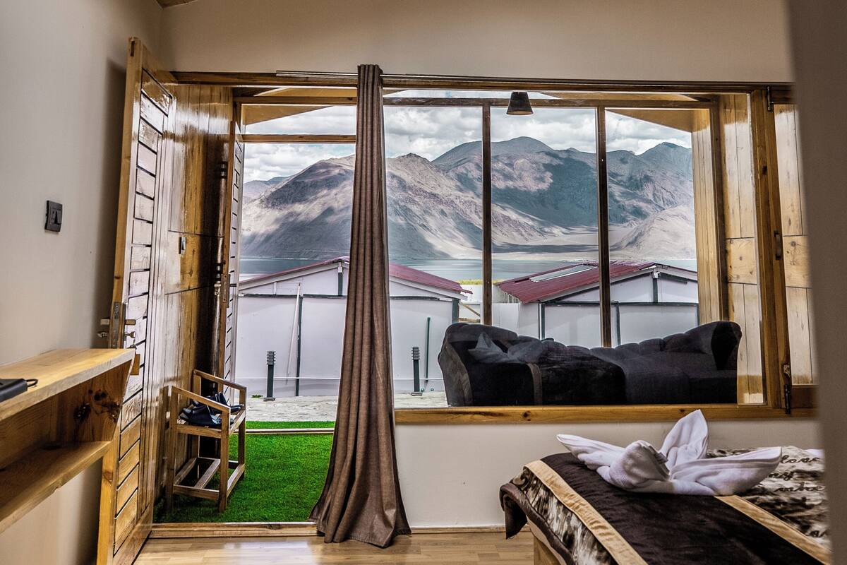 A room with a skylight, wooden ceiling, a bed, a desk, and a view of mountains.