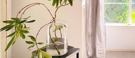 A room with a clear glass vase on a black table, a window with a view of greenery, and a door with a light switch.