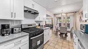 Una cocina moderna con armarios blancos, electrodomésticos de acero inoxidable y un comedor con mesa y sillas.
