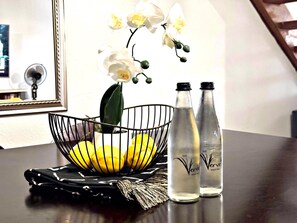 Una mesa con una cesta de mimbre que contiene limones, dos botellas de agua y una orquídea blanca.