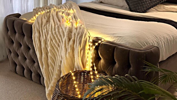 A bedroom with a tufted headboard, a white throw blanket, and a decorative light fixture.