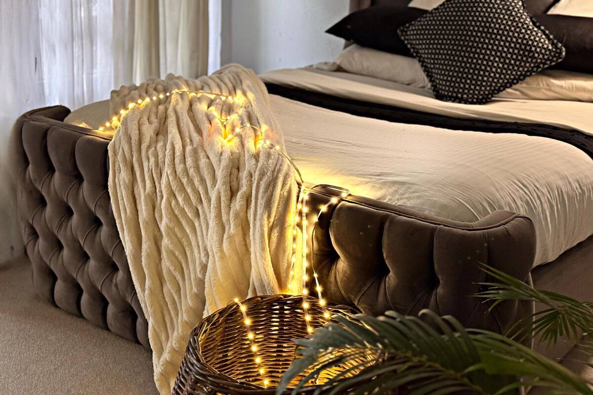 A bedroom with a tufted headboard, a white throw blanket, and a decorative light fixture.